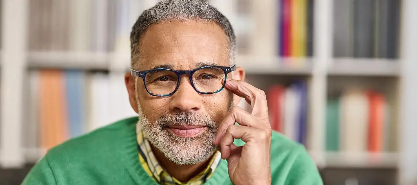 headshot of man in front of book shelf with glasses and hand on temple