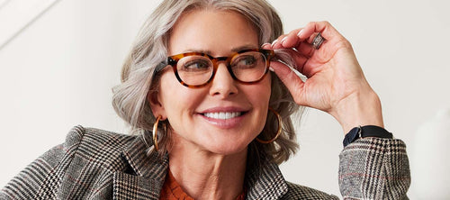woman with gray hair holding her glasses on her face and smiling