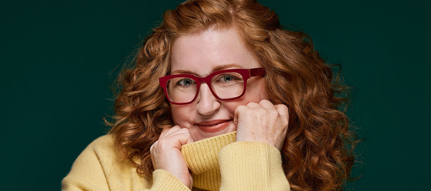 woman with red hair and red glasses in a yellow turtleneck