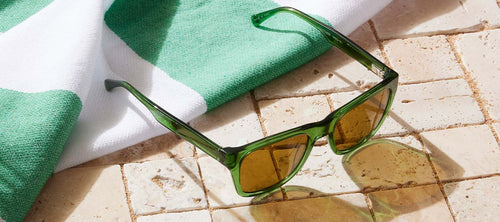 green frame polarized sunglasses next to a beach towel