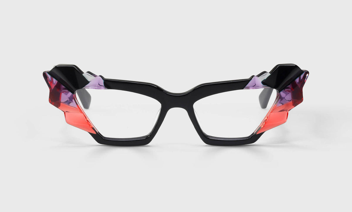 Cat-eye eyeglasses with black frame and sculptural mosaic temples in scarlet red, orchid purple, and asphalt black on gray background